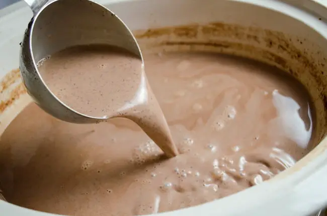 A ladle slowly pours creamy croc pot hot chocolate.