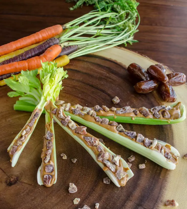 Celery sticks made into Ants on a Log, substituting dried dates for raisins. Colorful carrots and whole dates can be seen in the background.