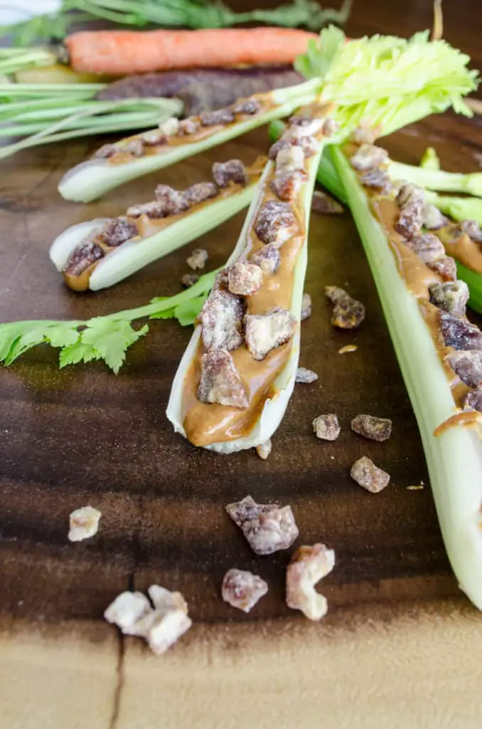 A closeup picture of a celery stick with leaves still attached at one end, filled with peanut butter and dried dates to make Ants on a Log.
