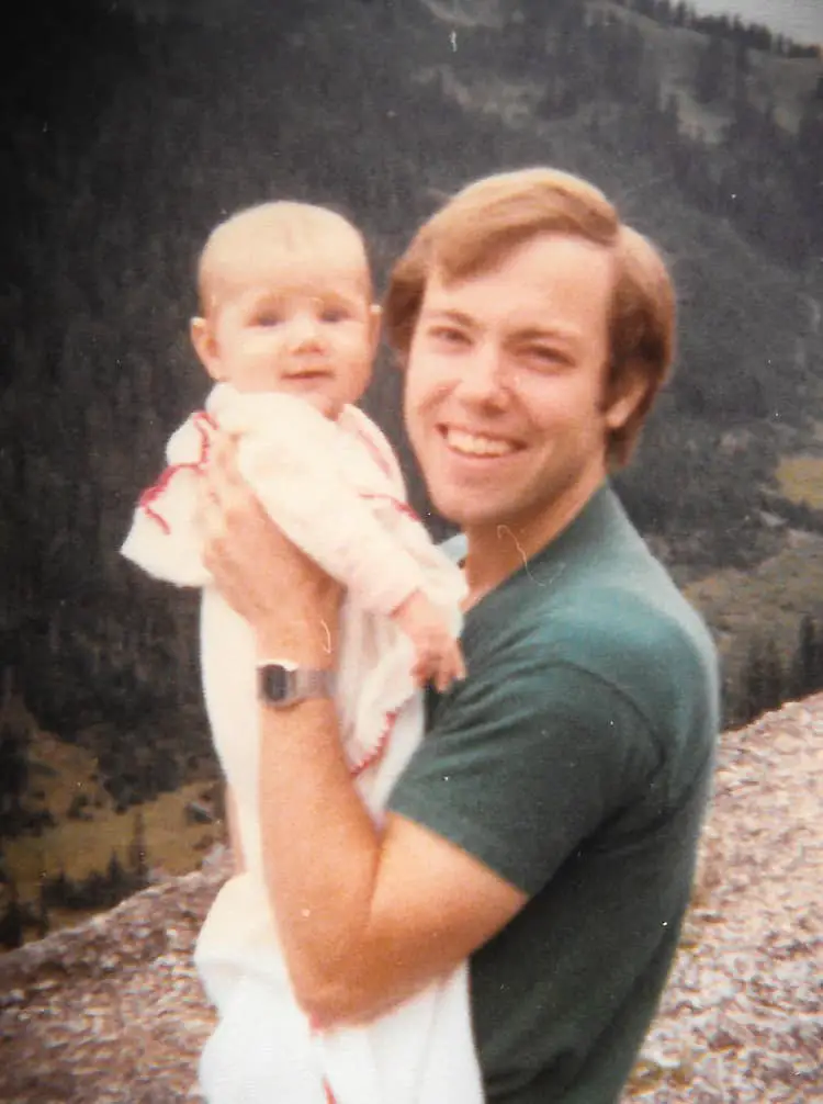 A father holding a baby with the mountains in the background.