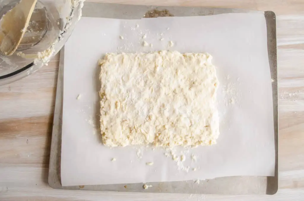 Biscuit dough shaped in a rectangle on a baking sheet for Quick Fluffy Coconut Biscuits.