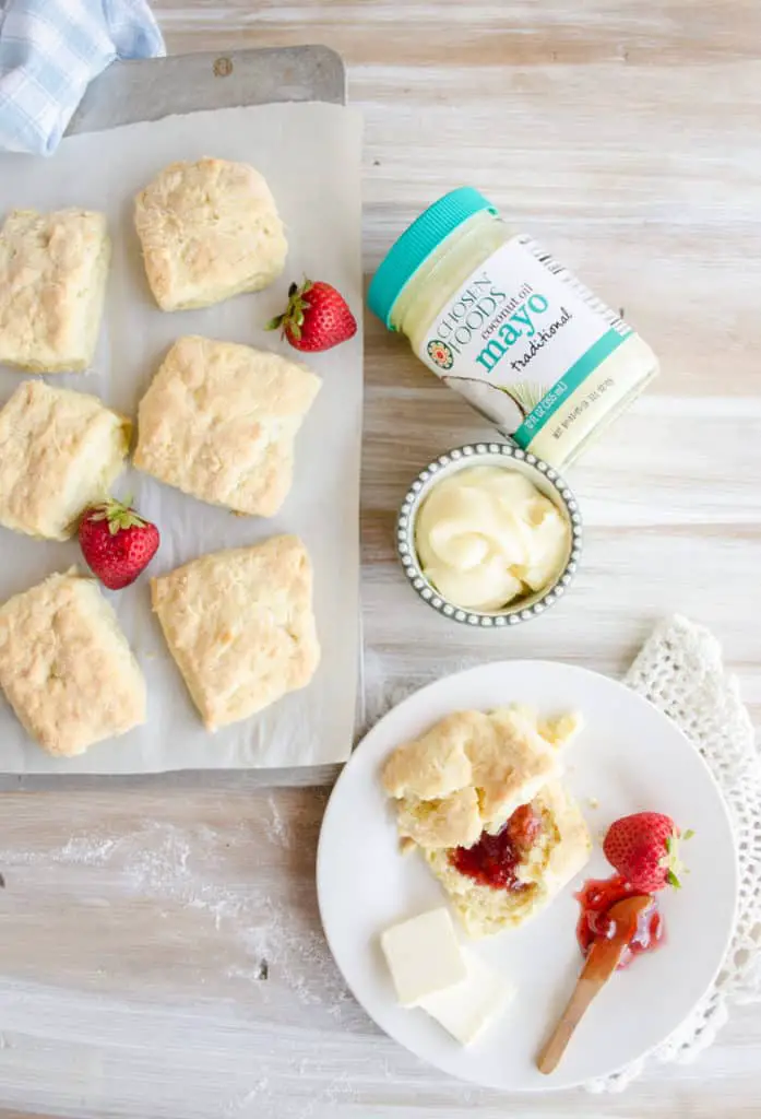 Quick Fluffy Coconut Biscuits sit on a baking sheet and a plate with strawberry jam.