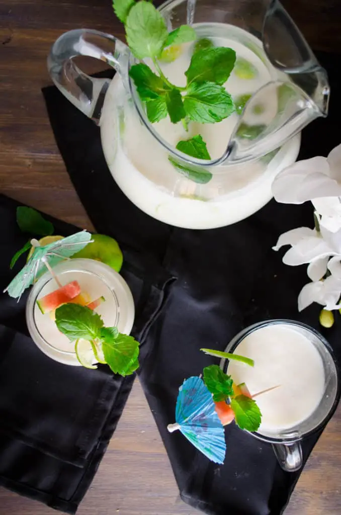 Crowd Pleasing Coconut Lime Mocktail fills glasses and a pitcher garnished with fruit and mint leaves.