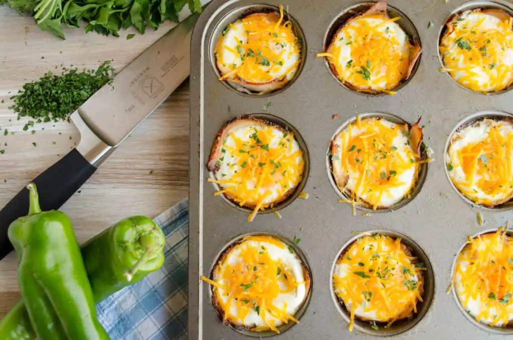 Green Chile Turkey Breakfast Cups sit in a muffin tin garnished with cheddar cheese and cilantro.