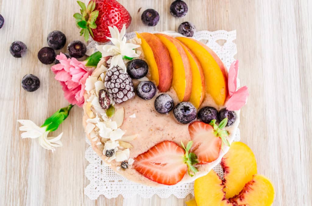 A Strawberry Peach Coconut Smoothie Bowl surrounded by fresh fruit pictured directly overhead.