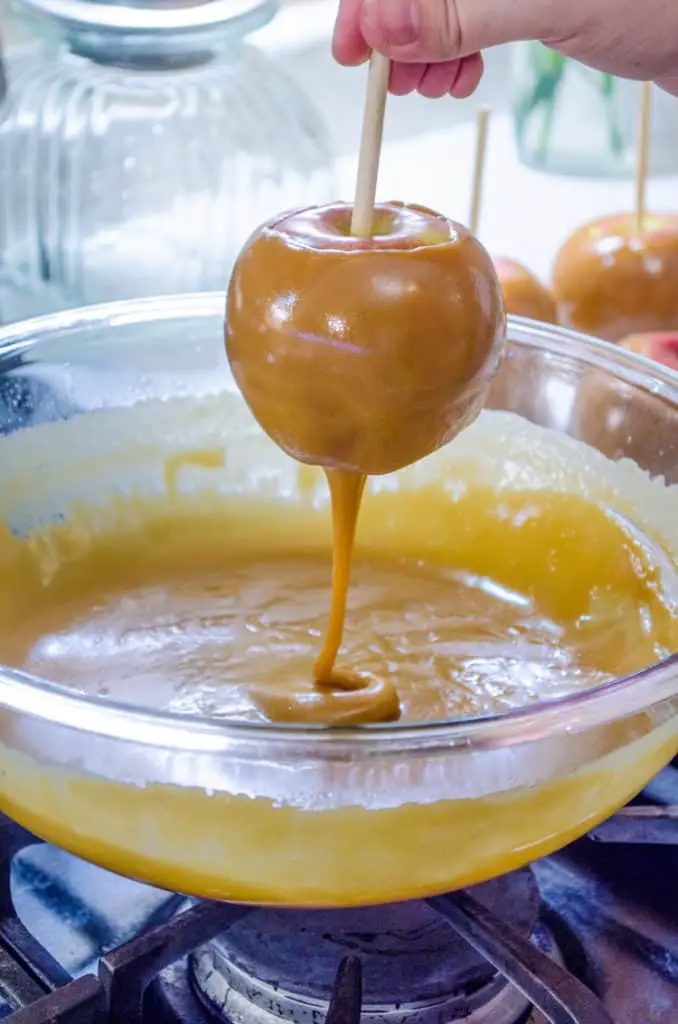 An apple dripping caramel back into a bowl filled with easy microwave caramel.