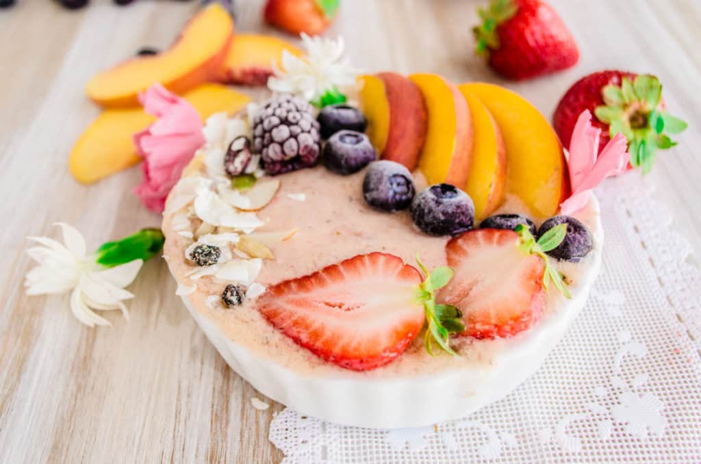 A closeup of a Strawberry Peach Coconut Smoothie Bowl topped with blueberries and coconut muesli.