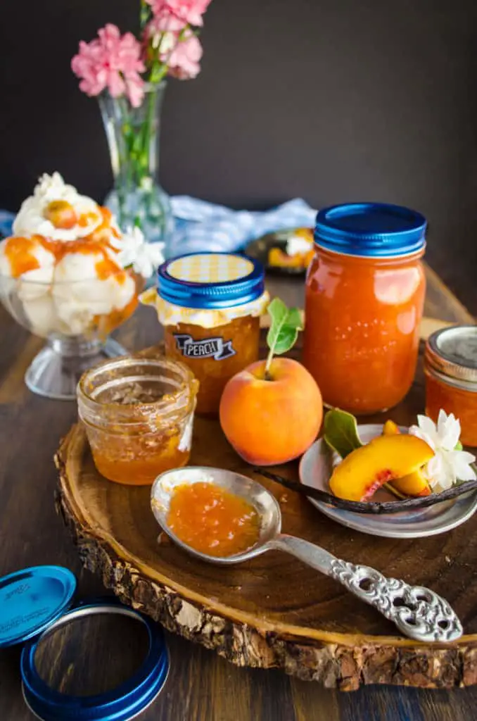 Homemade Vanilla Bean Peach Jam sits on a spoon surrounded with jars of jam and fresh peaches.