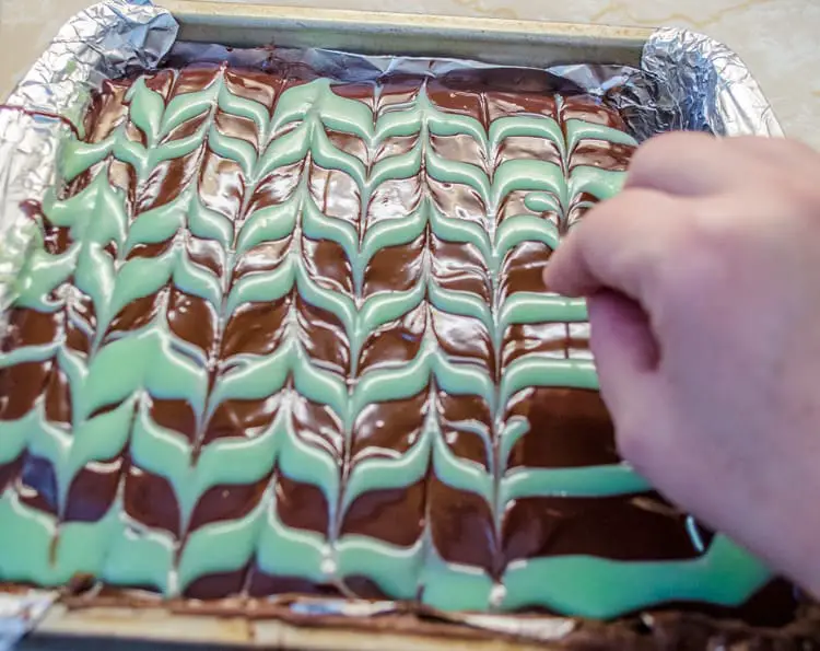 A toothpick is drawn through layers of white mint chocolate and semisweet chocolate to make a pretty chevron pattern on Fudgy Mint Brownies.