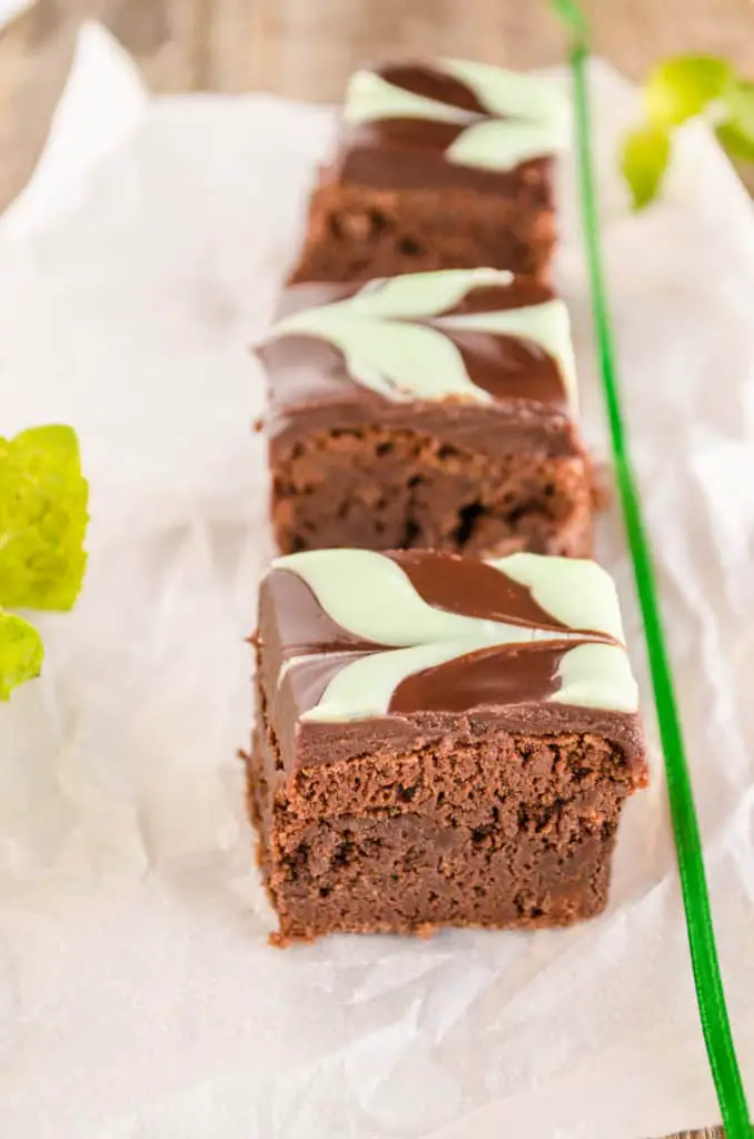 Fudgy Mint Brownies squares lined up in a row with mint and a green ribbon.