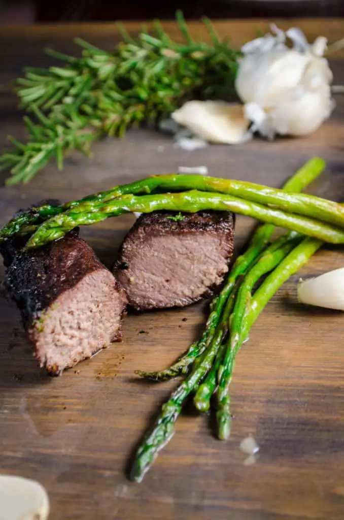 Grilled Elk Steak with Buttered Asparagus sliced to show the juicy meat inside. Asparagus sits to the side and on top of the steak.