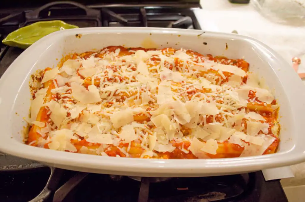 A baking dish full of Meatless Monday Cheese Stuffed Manicotti topped with grated cheese is ready for the oven.