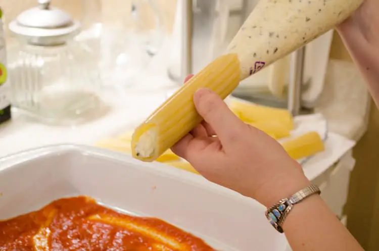 A manicotti shell is being piped (filled) with a cheese mixture for Meatless Monday Cheese Stuffed Manicotti.
