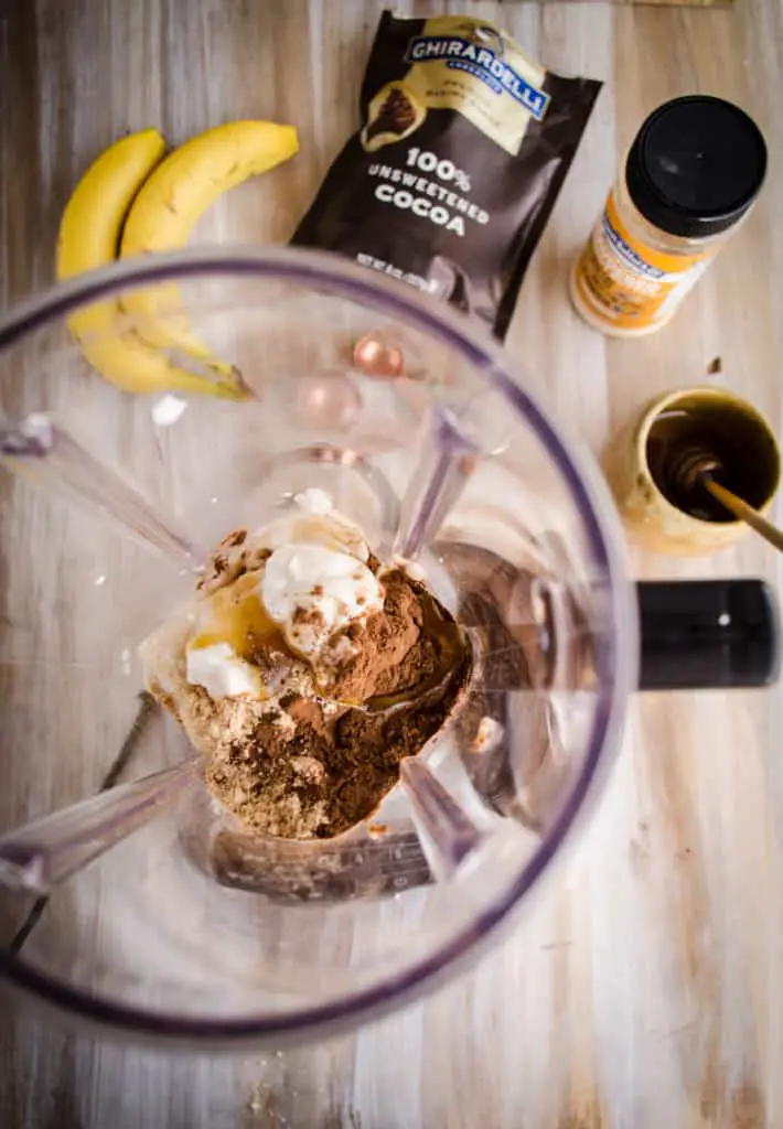 A top down view of the ingredients for a Peanut Butter Chocolate Banana Smoothie sit in a blender ready to be blended.