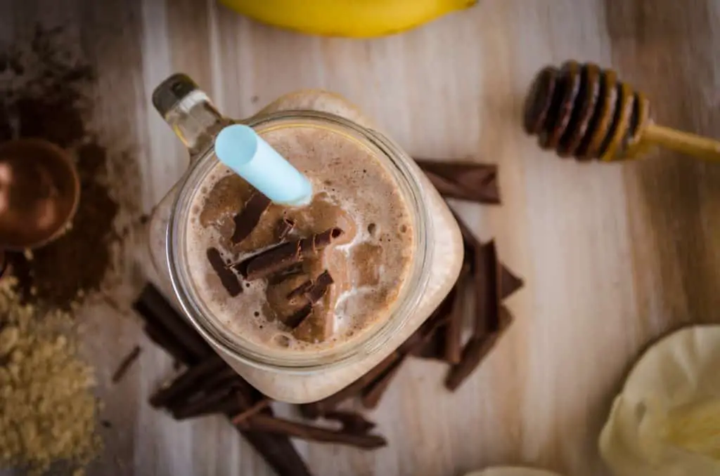 Closeup view of a Peanut Butter Chocolate Banana Smoothie topped with chocolate curls and a blue straw.