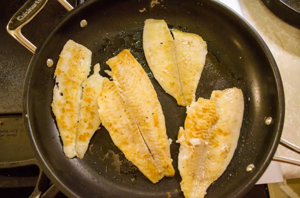 Golden sauteed fish sit in a non-stick pan for Fast Fish Dinner with Herbed Browned Butter.