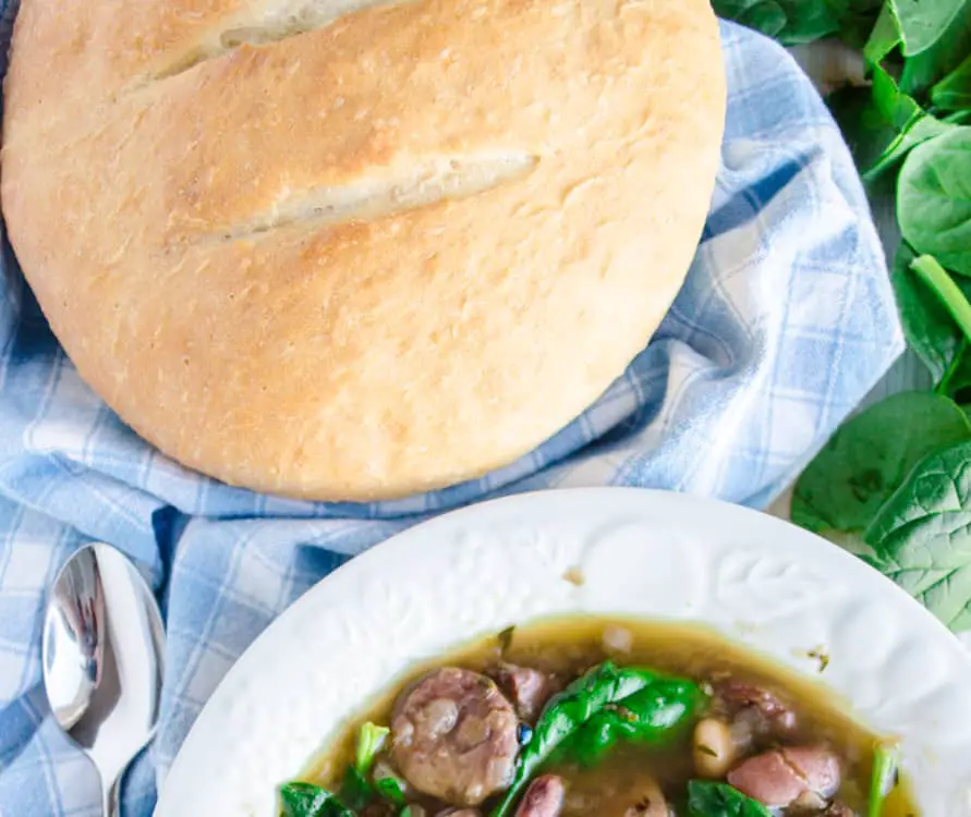 Quick Crusty Dinner Bread sits on a blue gingham kitchen towel with a bowl of soup.