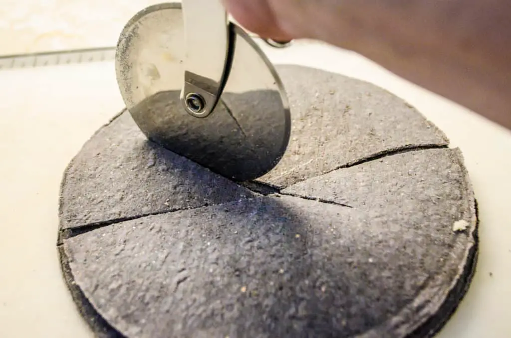 Blue corn tortillas are cut by a pizza cutter into wedges to make Crispy Baked Southwestern Tortilla Chips - The Goldilocks Kitchen