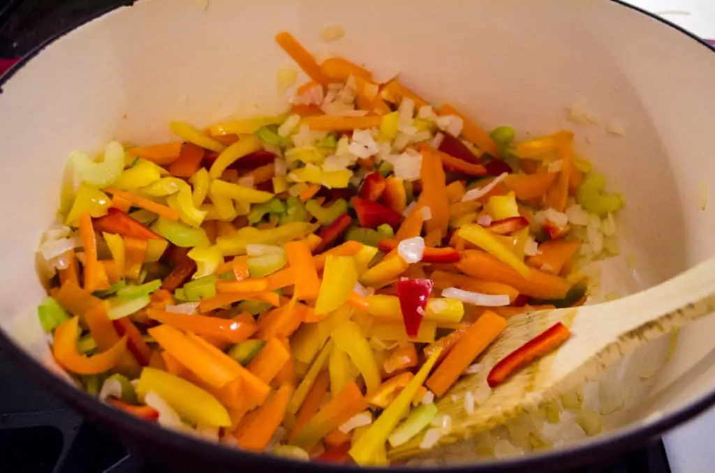 Chopped celery, bell pepper, onion, garlic and carrot are being cooked in a stovetop dutch oven for Meatless Monday Vegetable Rotini Soup.