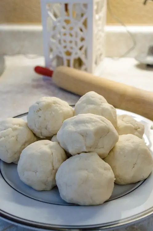 Balls of dough for Norwegian Lefse sit on a plate with a rolling pin in the background - The Goldilocks Kitchen