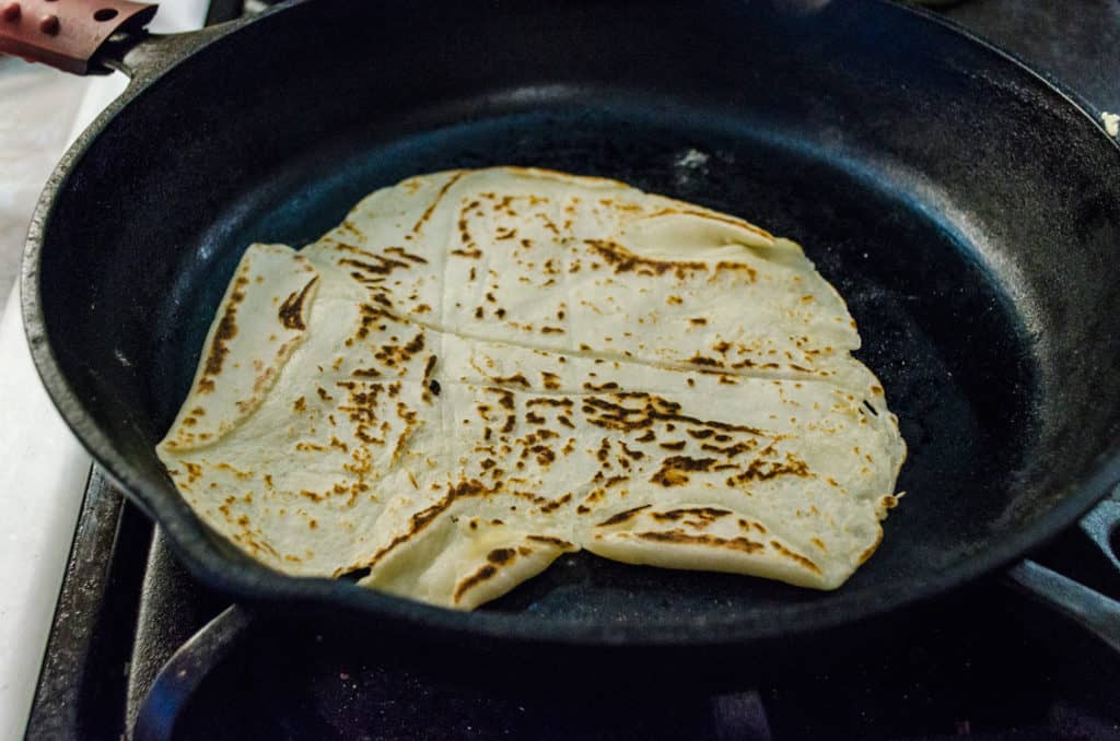 Spotty brown Norwegian Lefse cooks in a cast iron skillet - The Goldilocks Kitchen