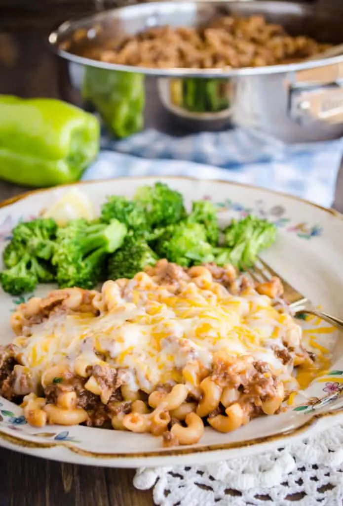 A serving of 30 Minute Chili Mac smothered in cheese sits on a plate with steamed lemon broccoli - The Goldilocks Kitchen