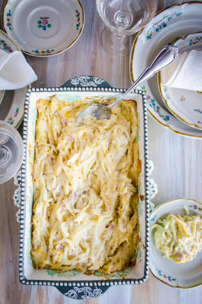 Cheesy Shredded Potato Casserole sits in a decorative baking dish on a table set for dinner - The Goldilocks Kitchen