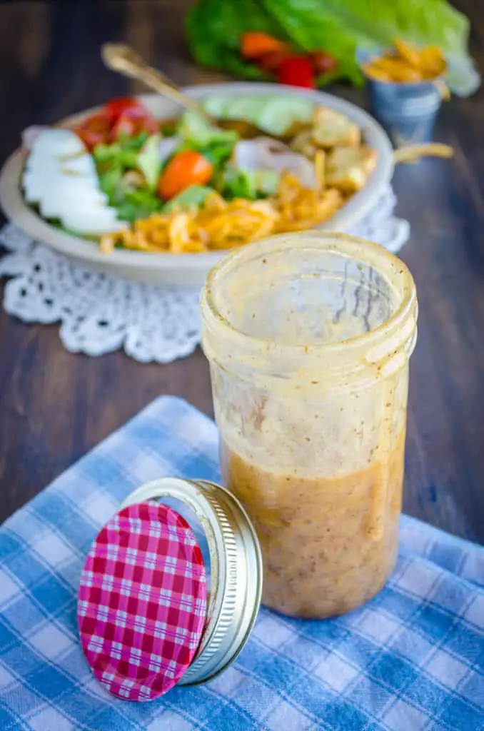 A glass mason jar with Ten Dollar Dressing in it sits in front of a chef's salad. - The Goldilocks Kitchen