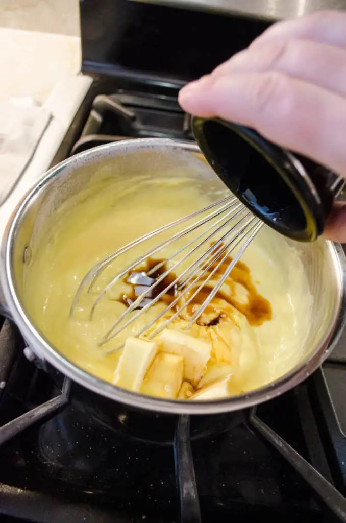 Pouring vanilla into custard cooking on a stovetop.