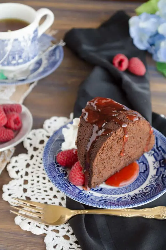 A slice of Chocolate Raspberry Bundt Cake is drizzled with raspberry filling and garnished with whipped cream and fresh raspberries. - The Goldilocks Kitchen
