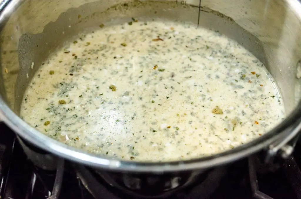 A white cream sauce flavored with shallot, garlic and thyme cooks in a medium saucepan for Creamy Stuffed Fish Florentine - The Goldilocks Kitchen