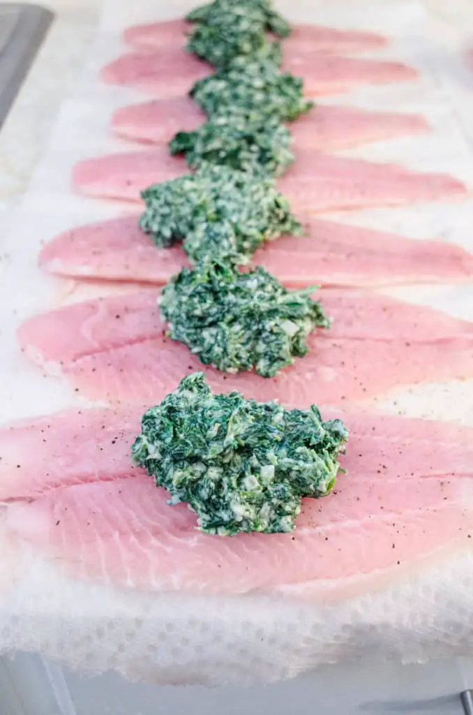 Raw Swai fish fillets are lined up in a row, each topped with a mound of spinach parmesan stuffing for Creamy Stuffed Fish Florentine - The Goldilocks Kitchen