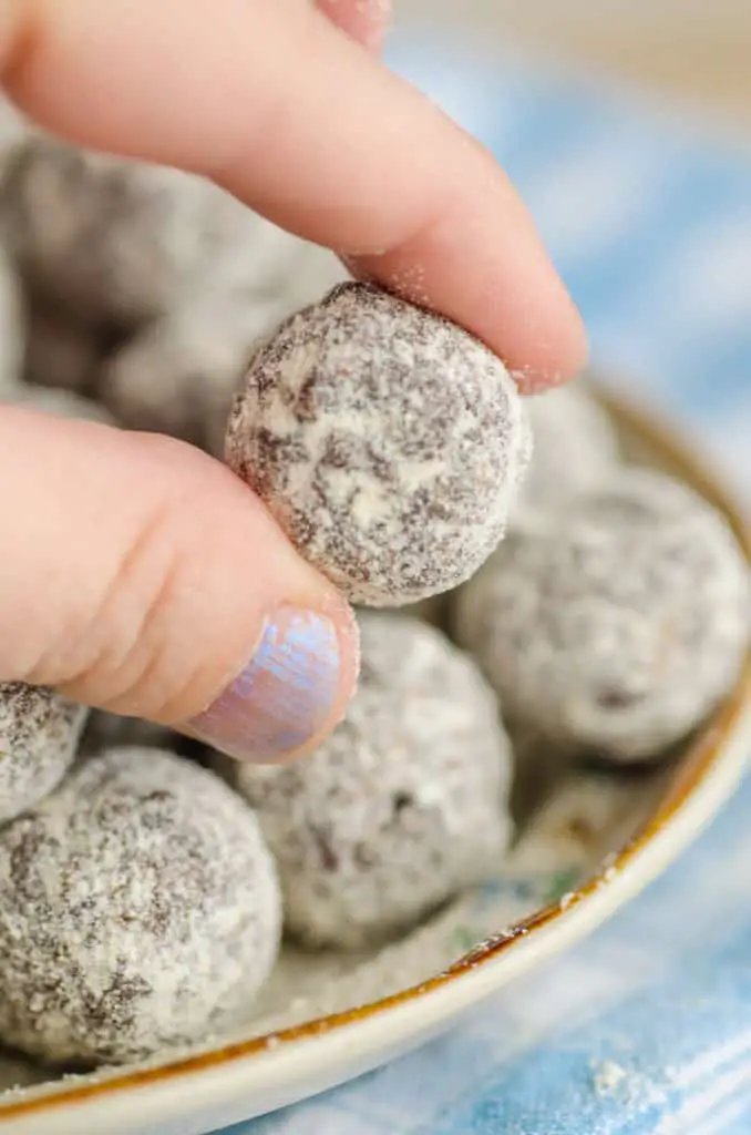 A Chocolate Mint Energy Bites ball is held close to the camera by fingers to show the texture - The Goldilocks Kitchen