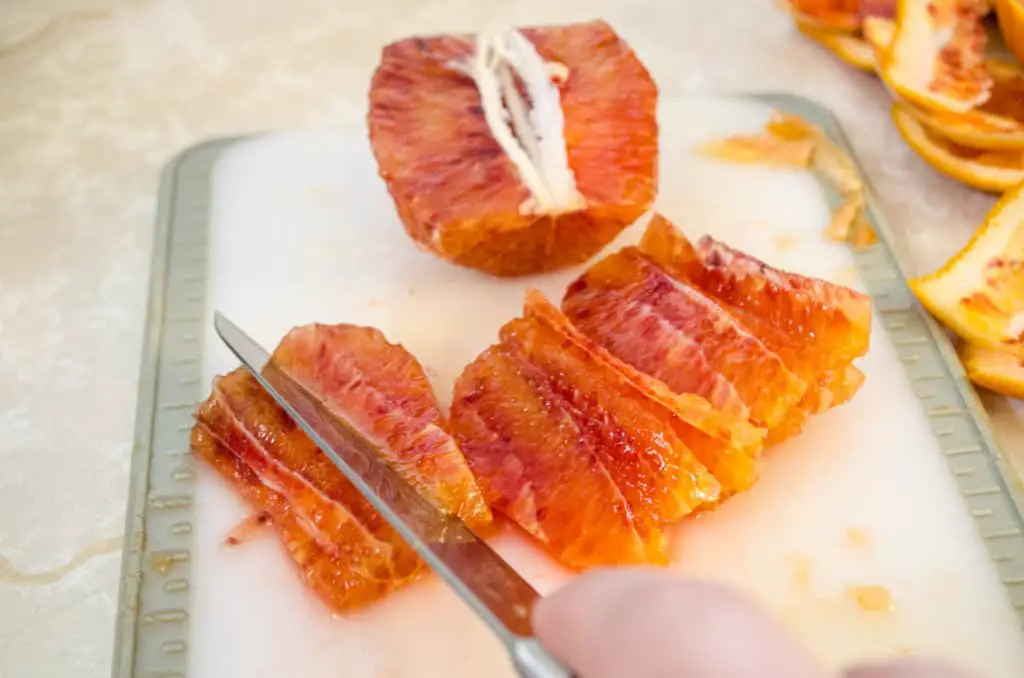 Blood orange is segmented into thin wedges with a knife on a cutting board for Feta Citrus Salad - The Goldilocks Kitchen