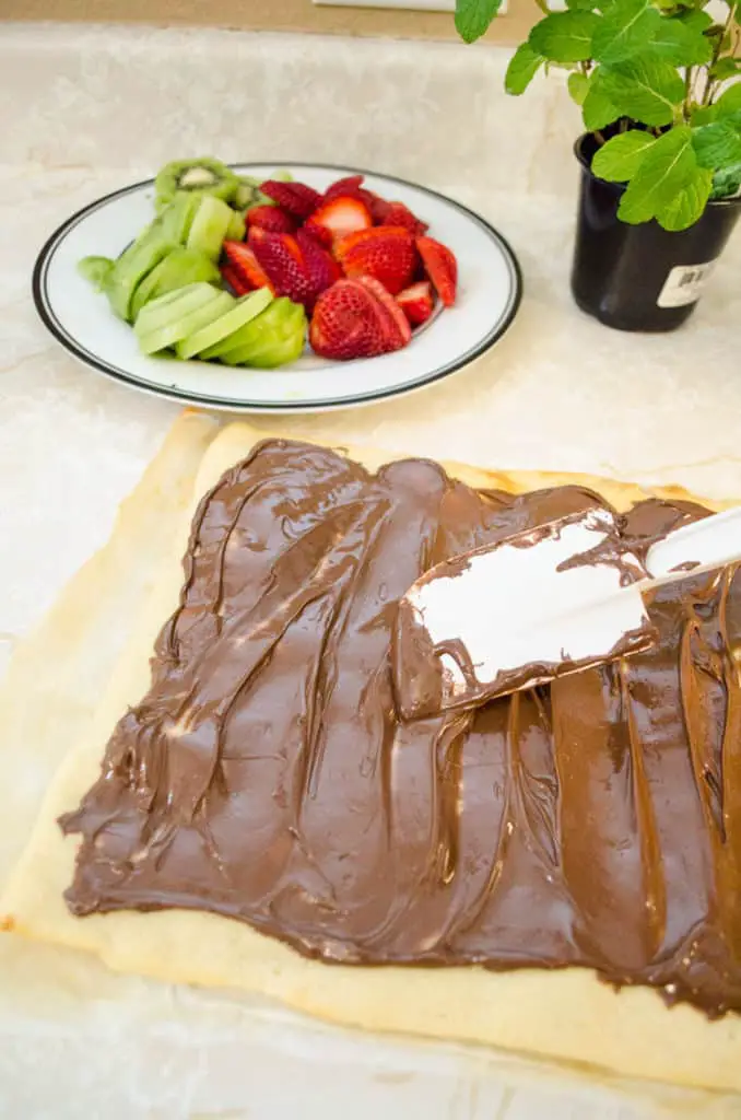 A rectangular pizza crust is spread with Nutella for Nutella Pizza - The Goldilocks Kitchen