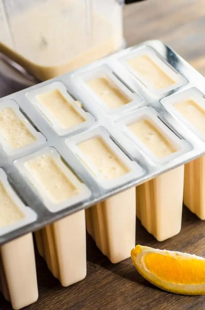 A popsicle mold is full of orange liquid to make Orange Creamsicle Smoothie Pops - The Goldilocks Kitchen