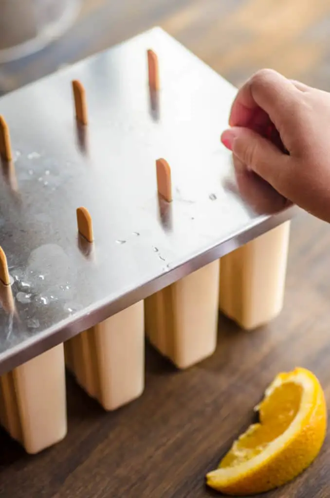 Wooden sticks are inserted into a popsicle mold for Orange Creamsicle Smoothie Pops - The Goldilocks Kitchen
