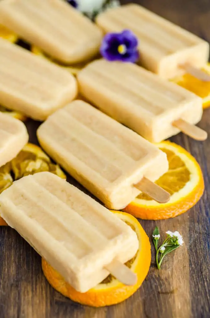Orange Creamsicle Smoothie Pops sit on slices of oranges surrounded by white and purple flowers - The Goldilocks Kitchen 