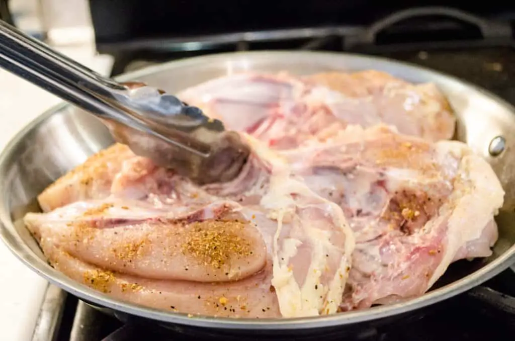 Raw bone-in, skin-on chicken breast is browned in a large stovetop skillet for Weeknight Roasted Chicken Breast with Red Potatoes - The Goldilocks Kitchen