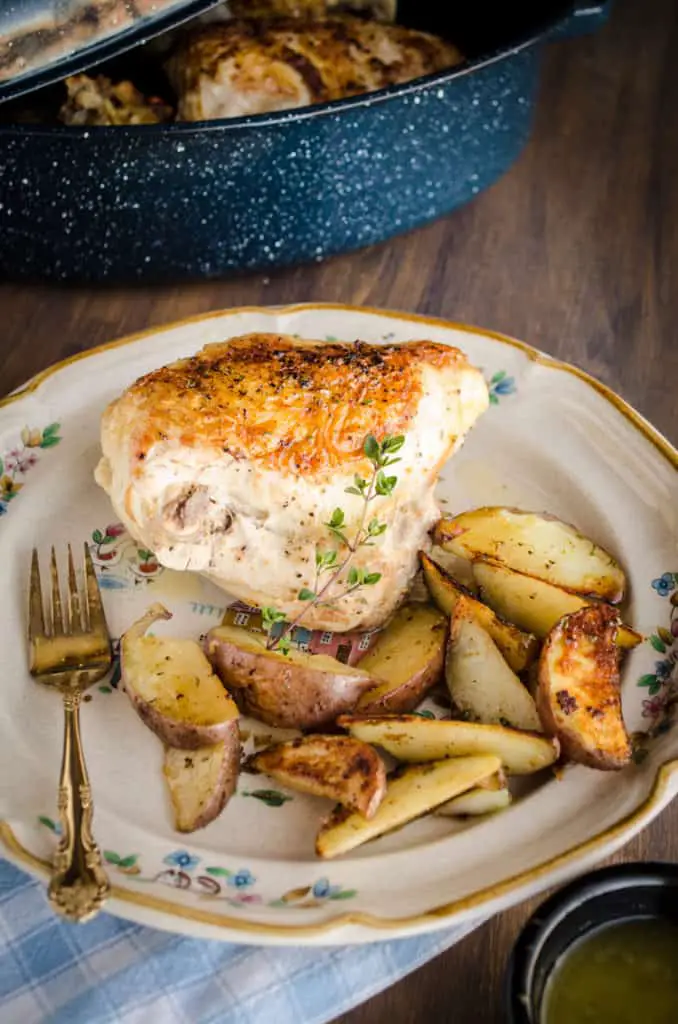 A roasted chicken breast sits on a decorative plate with browned and seasoned red potato wedges garnished with a sprig of thyme for Weeknight Roasted Chicken Breast with Red Potatoes recipe - The Goldilocks Kitchen