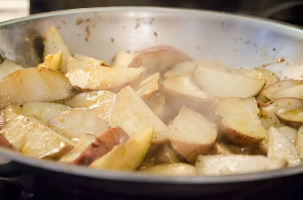 Red potato wedges are cooked in a skillet for Weeknight Roasted Chicken Breast with Red Potatoes- The Goldilocks Kitchen
