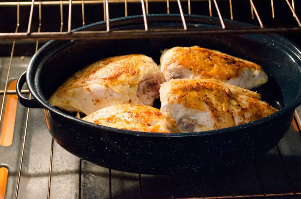 Golden browned chicken breast is nestled into a roasting pan skin side up, in an oven for Weeknight Roasted Chicken Breast with Red Potatoes - The Goldilocks Kitchen