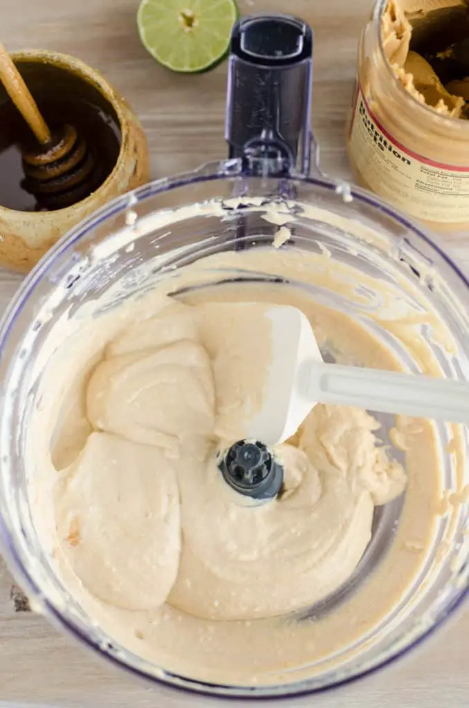 The bowl of a food processor containing Silky Peanut Butter Dip just after being made, and is scooped out with a white spatula. - The Goldilocks Kitchen