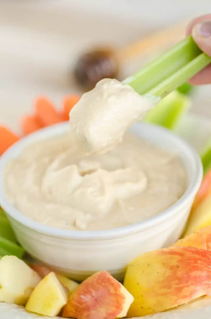 A celery stick is dipped into Silky Peanut Butter Dip - The Goldilocks Kitchen