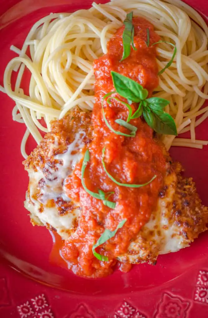 A serving of Easy Chicken Parmesan with a side of spaghetti sits on a red plate.