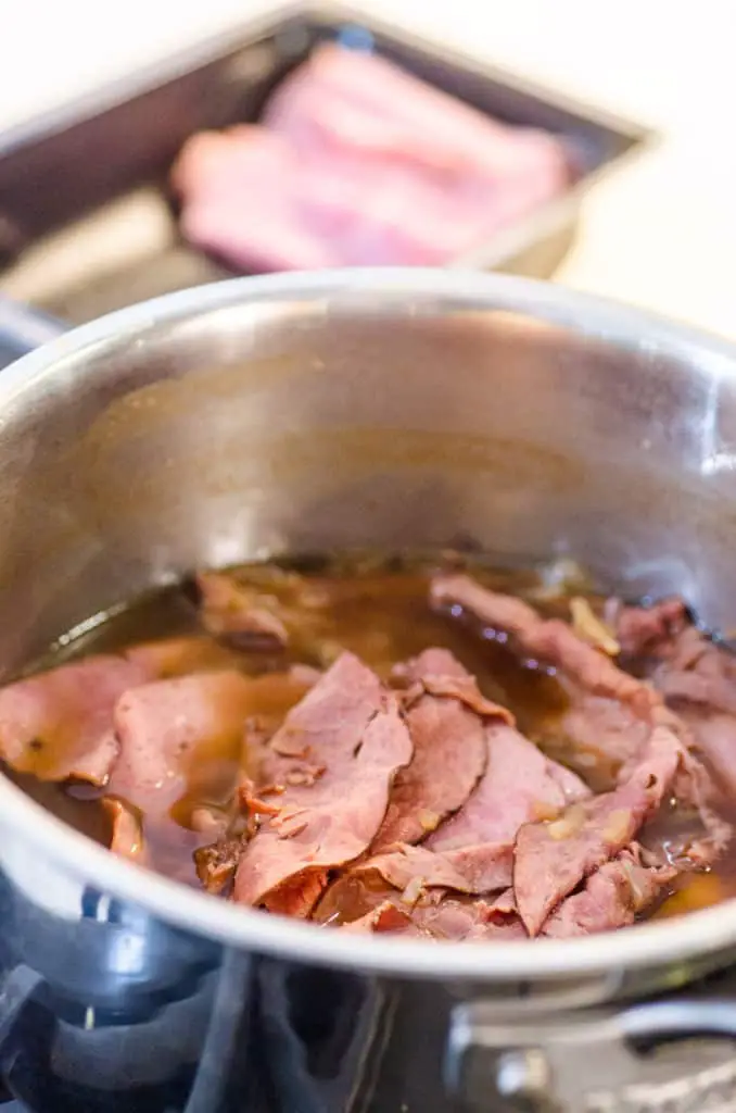 A close up of a pot containing sliced roast beef soaking in beef au jus for 30 Minute French Dip with Au Jus Sandwiches.