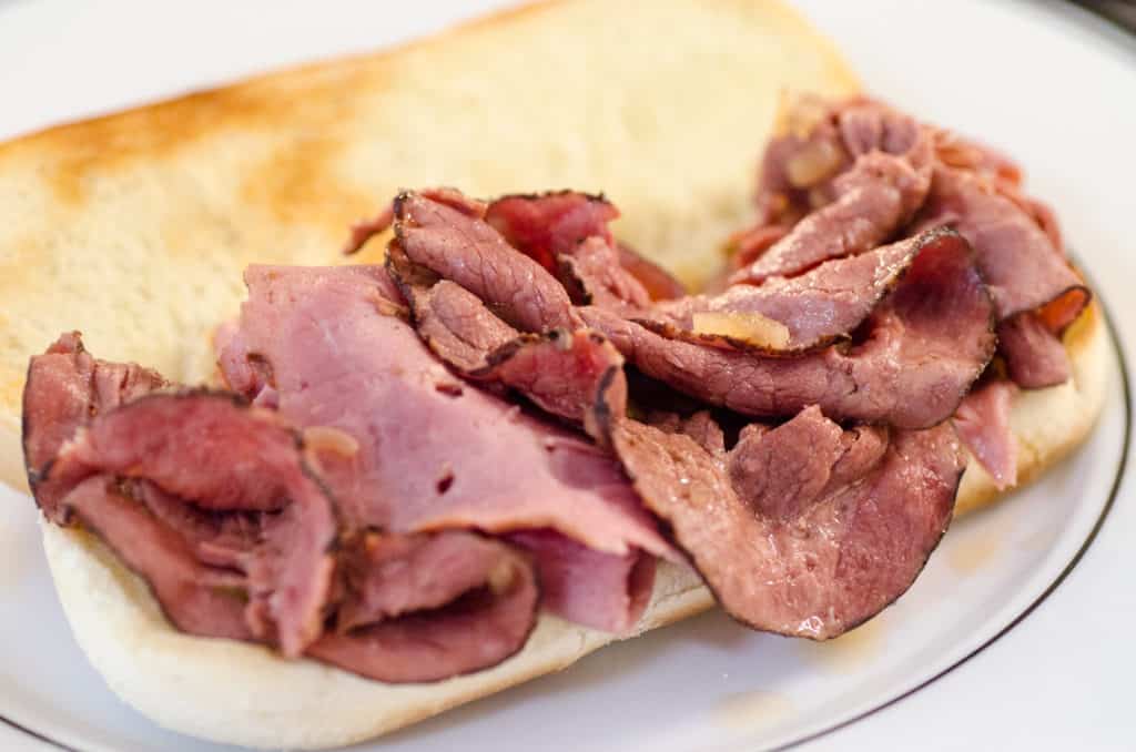 A French Dip with Au Jus sandwich full of roast beef waits to be topped with cheese.