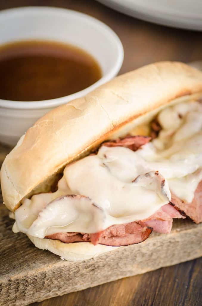 A fresh made French Dip with Au Jus sandwich sits next to a small cup of au jus.