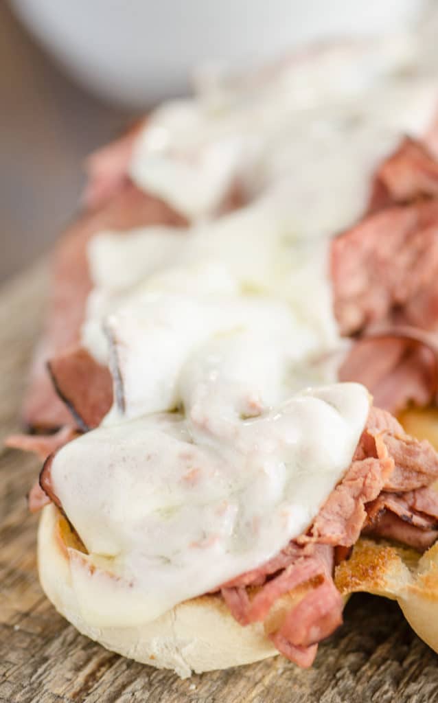 French Dip with Au Jus sandwich closeup with melted provolone cheese on top of sliced roast beef.