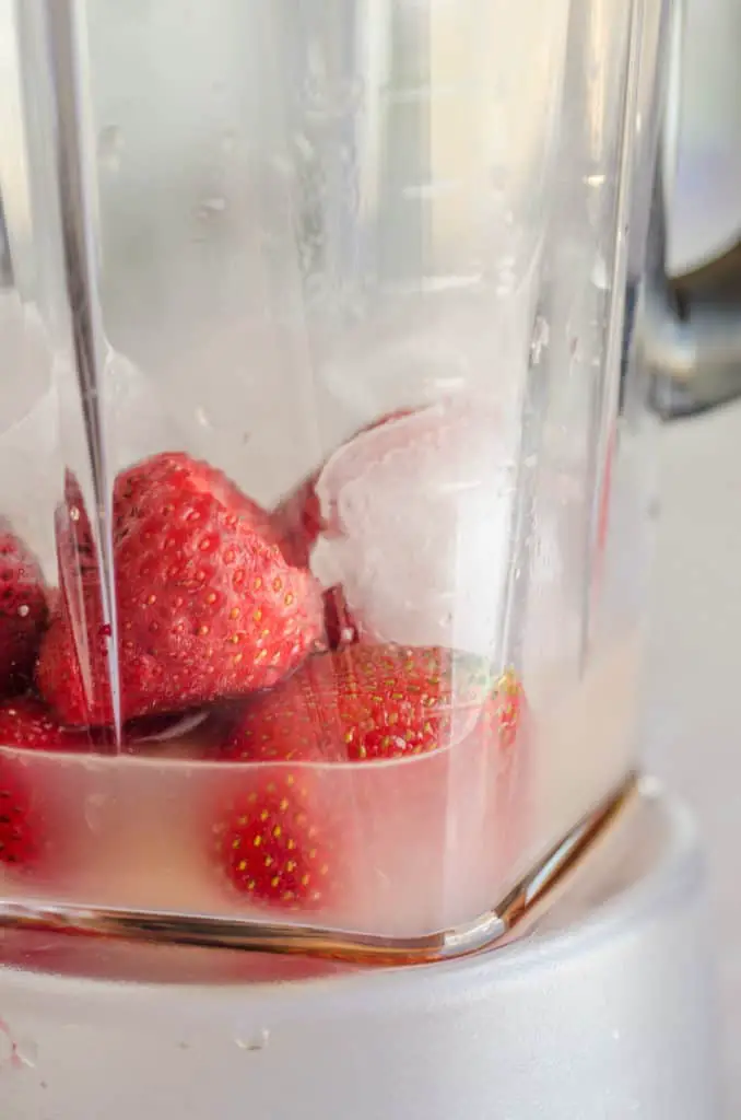 Strawberries, ice, water, agave nectar, and orange extract sit in a blender for making Fresh Virgin Strawberry Margaritas.